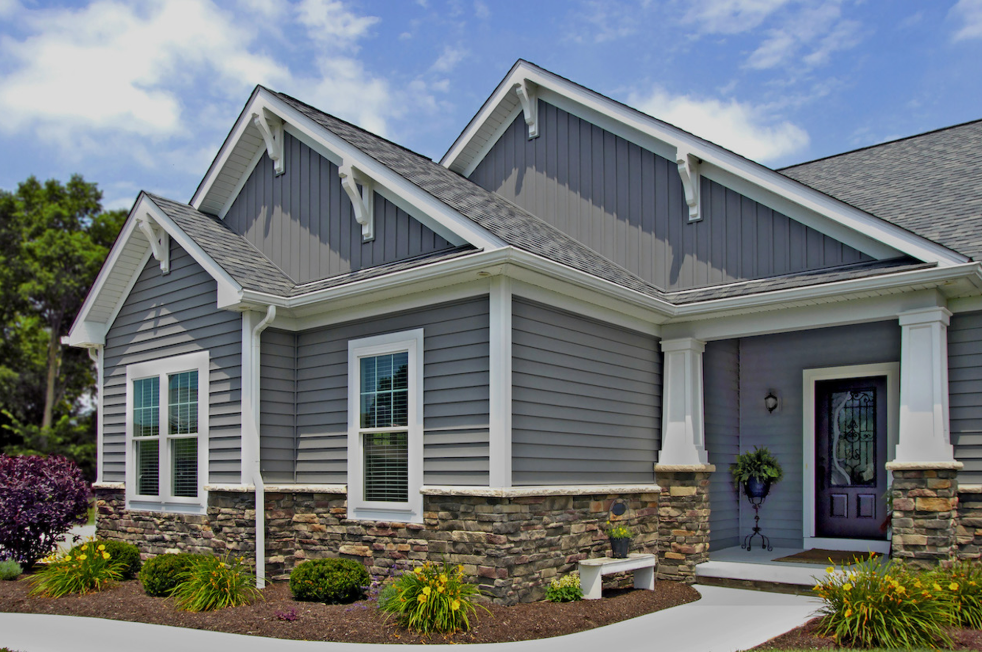 Front view of a gray suburban house with stone veneer, white trim, and a covered porch against a blue sky.